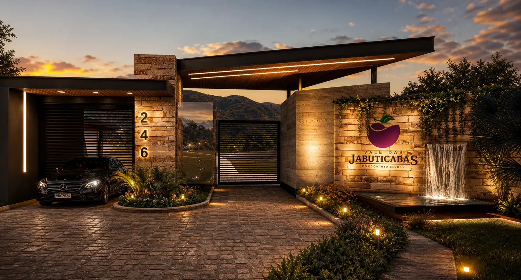 Portaria do Vale das Jabuticabas ao entardecer, com muro de pedra, cascata iluminada e logo do empreendimento (imagem ilustrativa)
